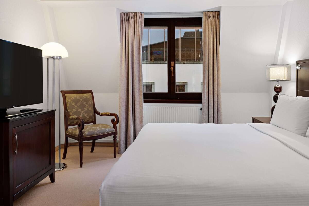 A hotel room with a bed, a chair, a television, and a window with curtains.