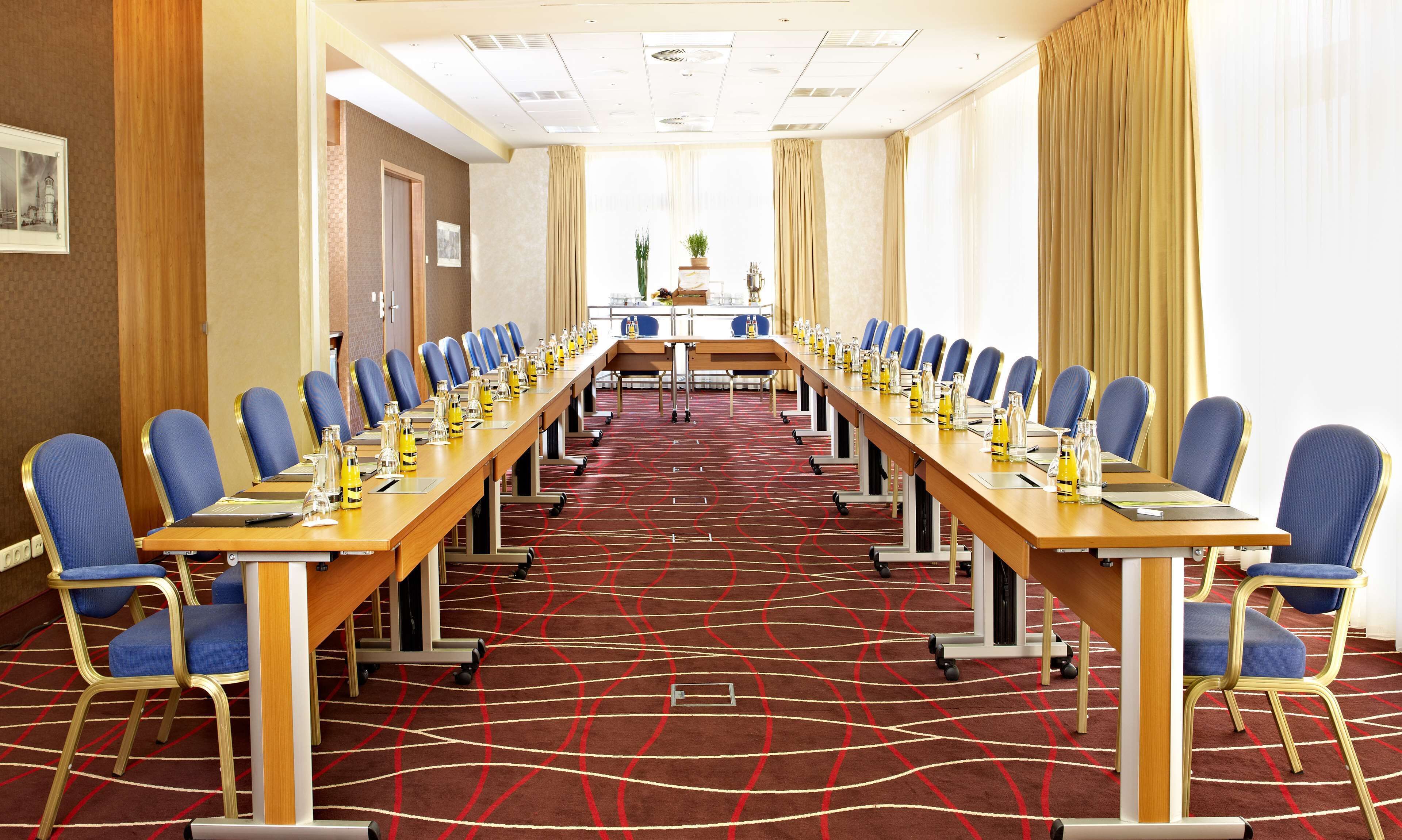 Ein Konferenzraum mit langem Tisch, blauen Stühlen und einem roten Teppich.