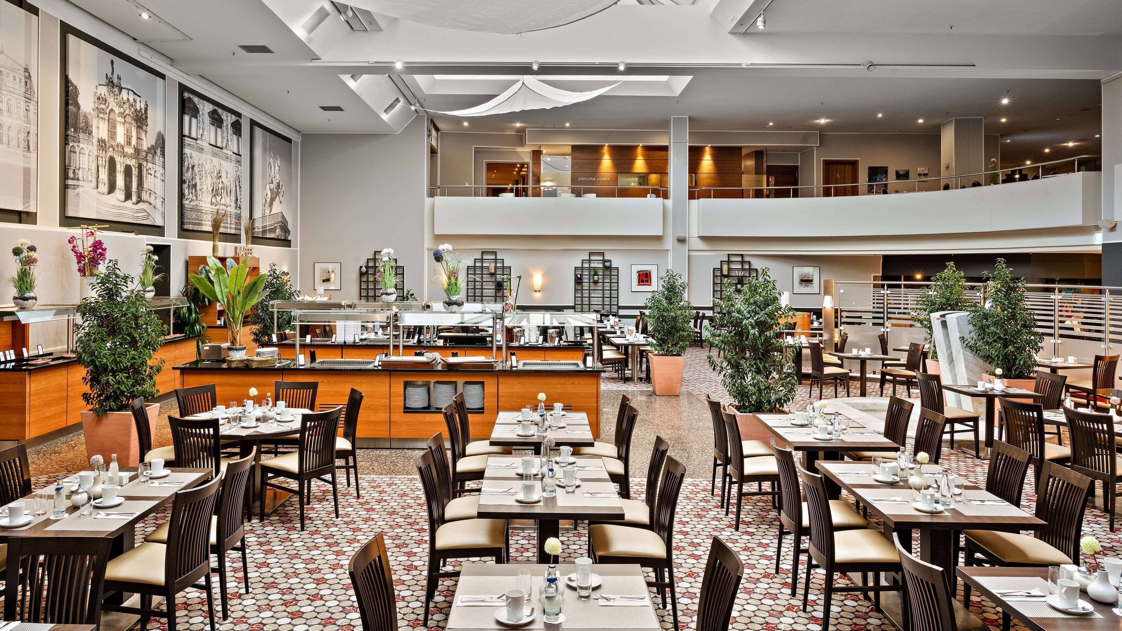 A modern hotel lobby with a central bar, dining area, and a mezzanine level.