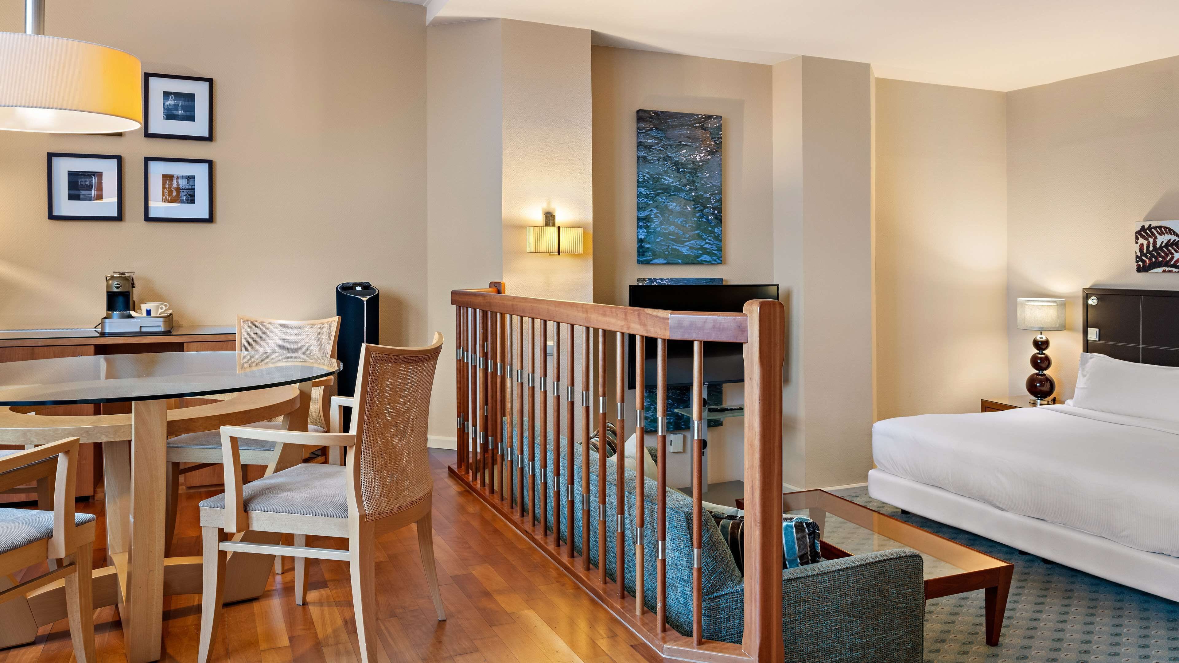 A hotel room with a dining area, a bed, a TV, and artwork on the walls.