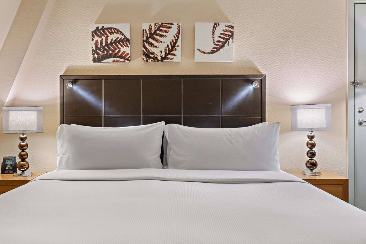 A neatly made bed with white linens, flanked by two bedside tables with lamps and a clock, against a wall with three framed botanical prints.