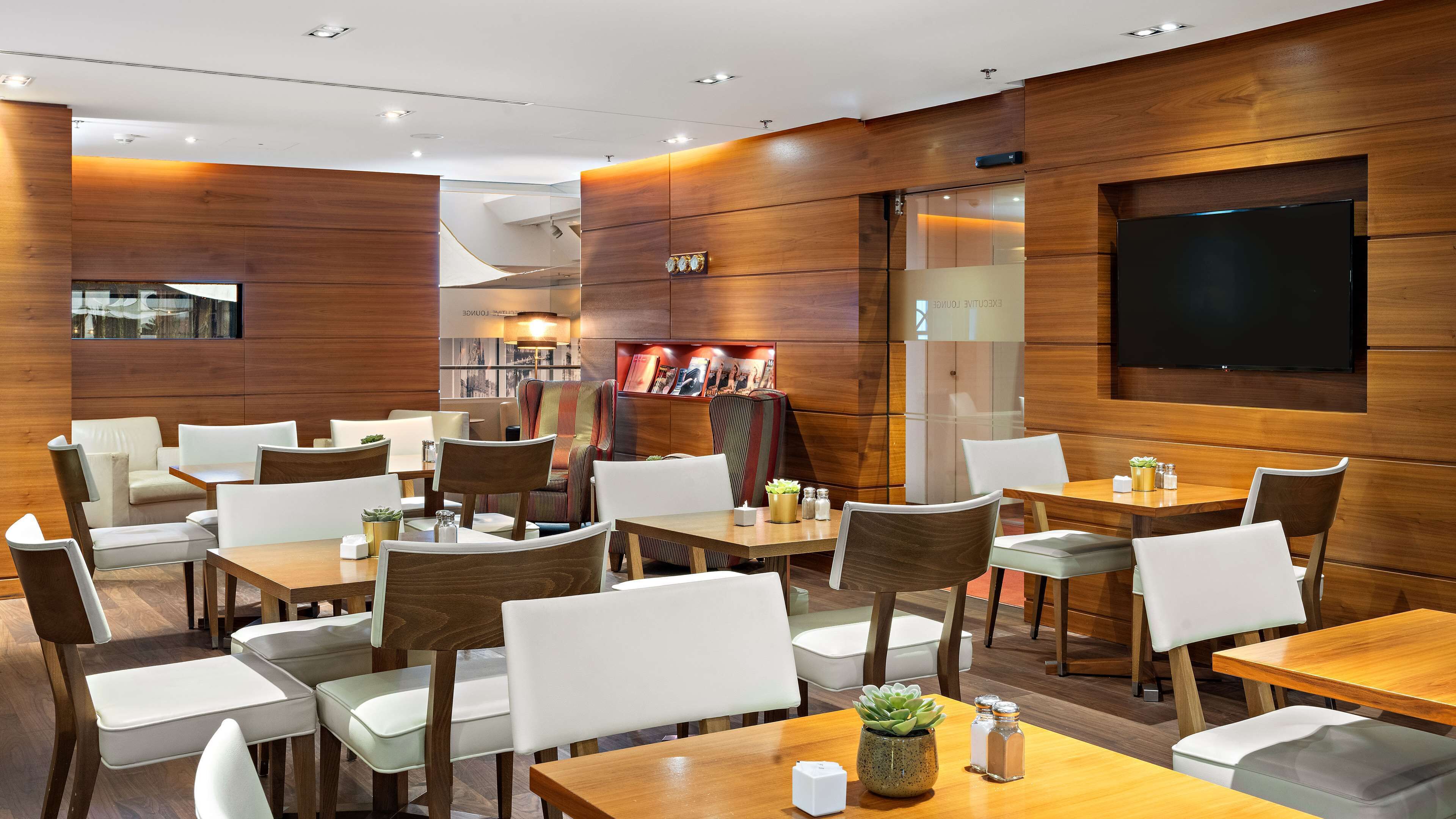 Un restaurante moderno con paneles de madera, varias mesas y sillas, y un televisor de pantalla plana montado en la pared.
