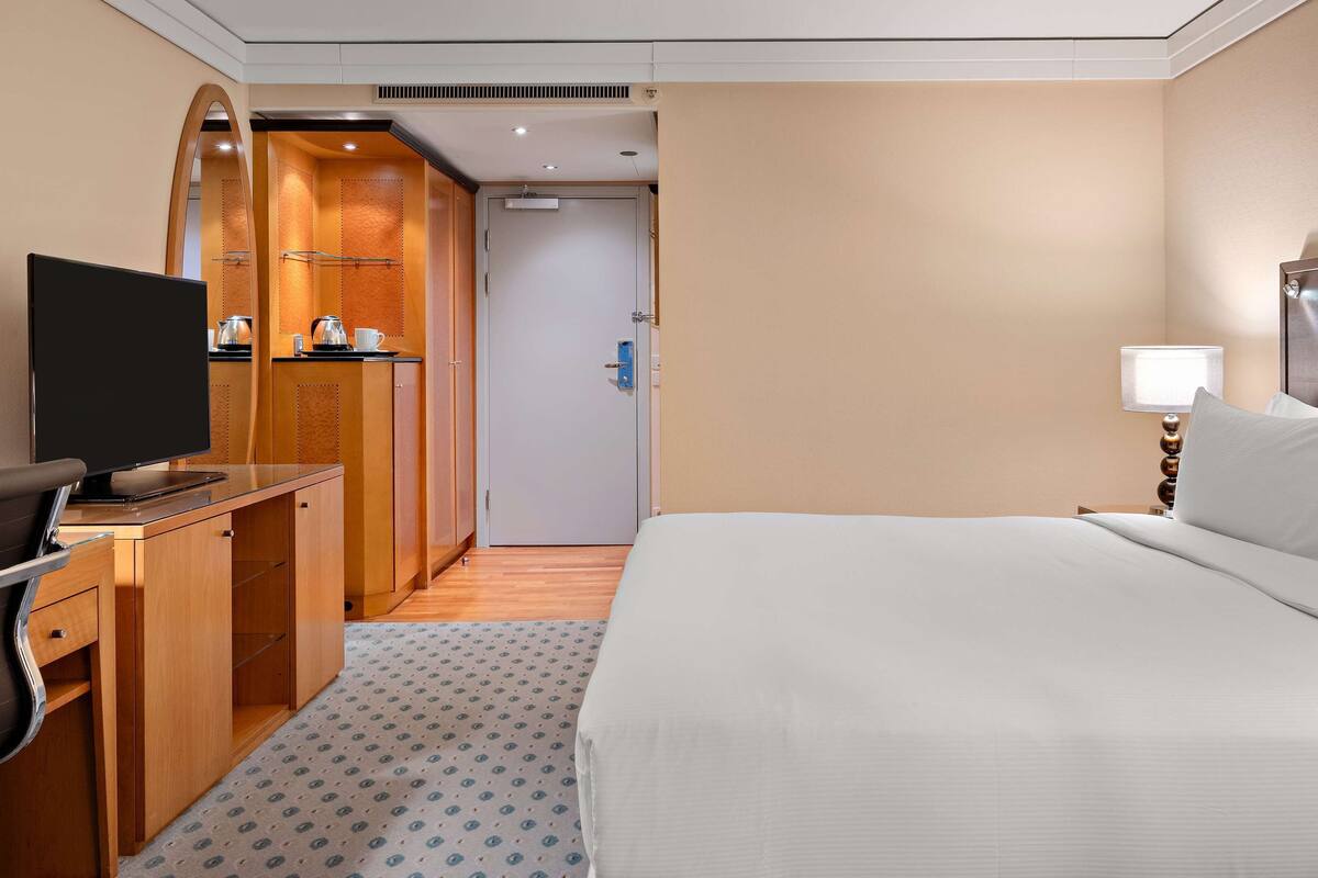 A hotel room with a bed, a desk with a TV, a mirror, and a wardrobe.