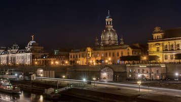 Un edificio histórico con una cúpula destacada y una estatua en la parte superior, ubicado junto a un río con un puente y un muelle para barcos.