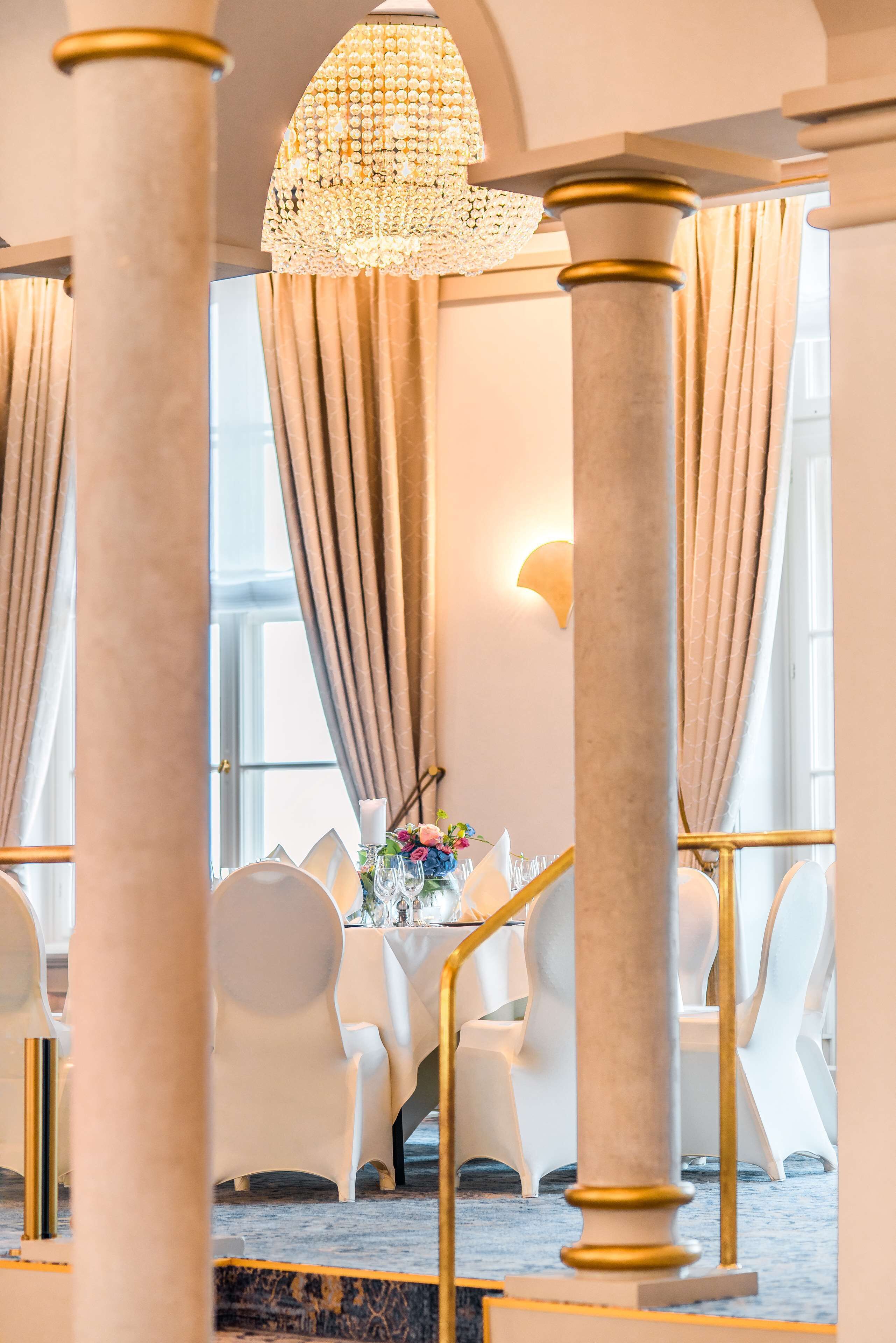 A formal dining area with white chairs, a table set with a floral centerpiece, and a chandelier.