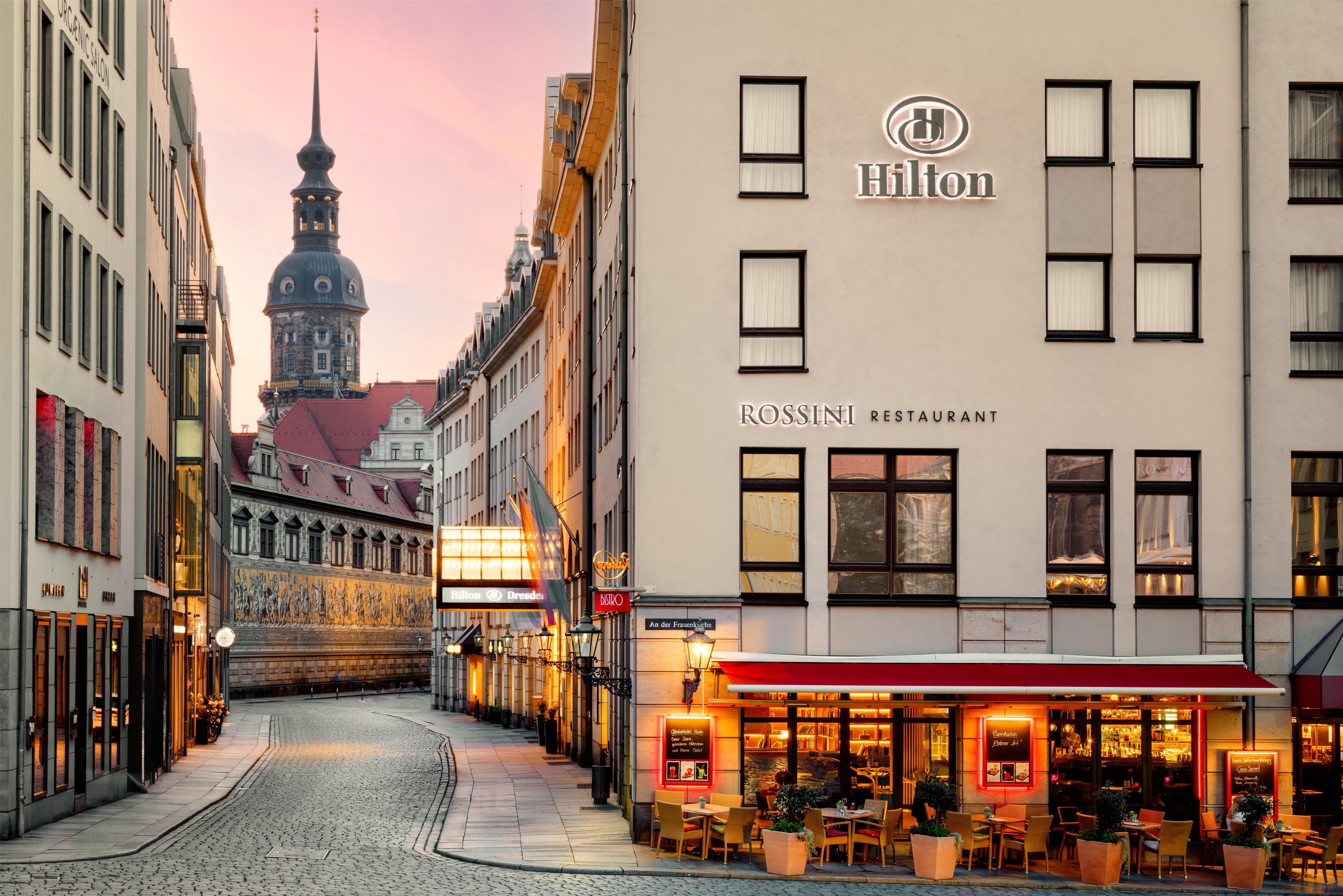 A street view with a hotel and restaurant named 'Rossini' and 'Hilton' with outdoor seating.