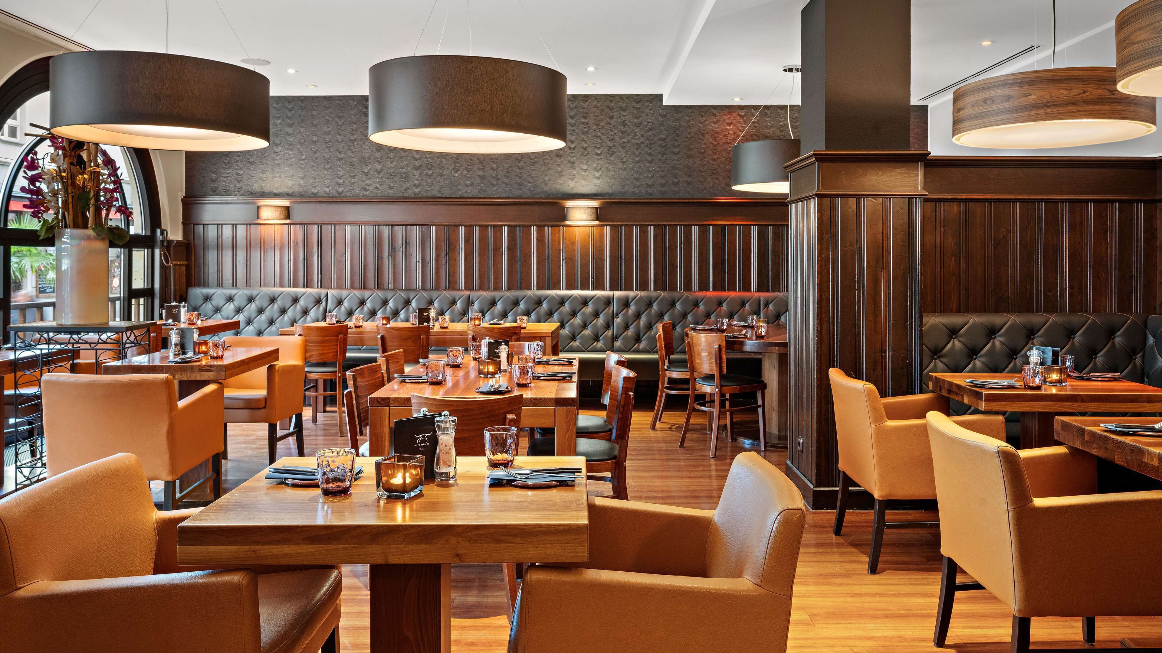 A restaurant with wooden tables and chairs, leather booths, and hanging pendant lights.