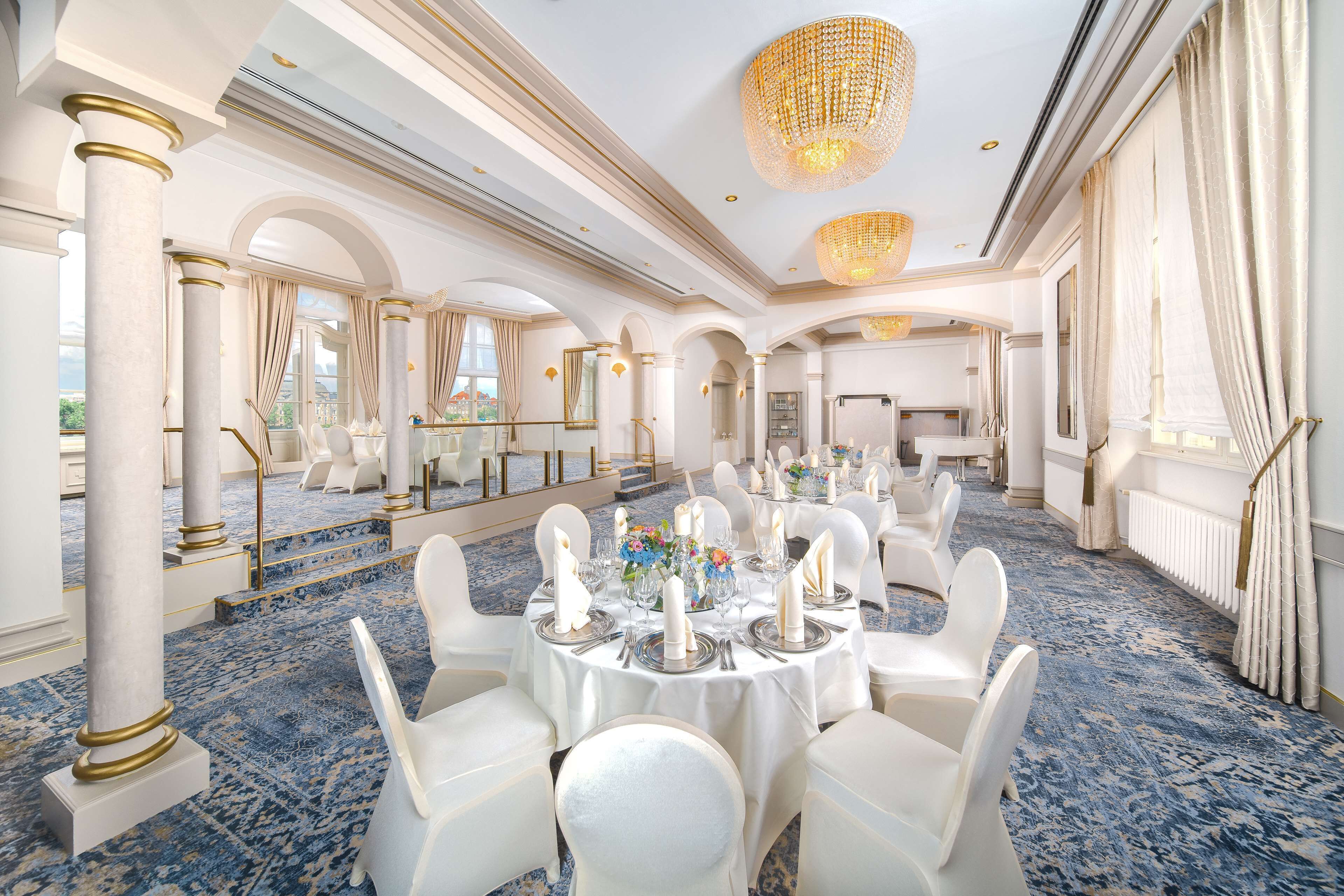 Une salle à manger élégante, avec des tables rondes, des chaises blanches et des lustres.