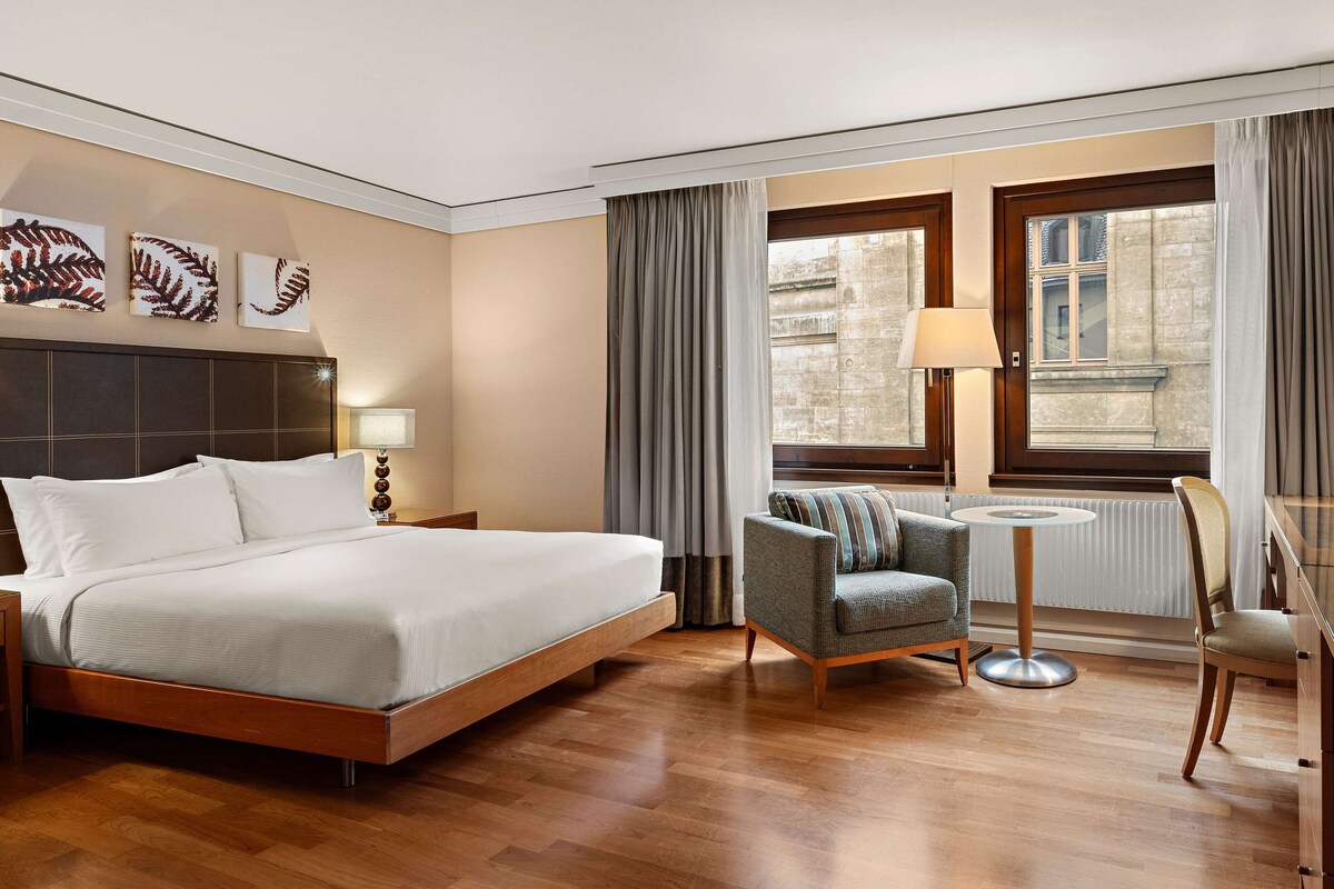 Habitación de hotel con una cama grande, un escritorio con silla, una mesita y un televisor.