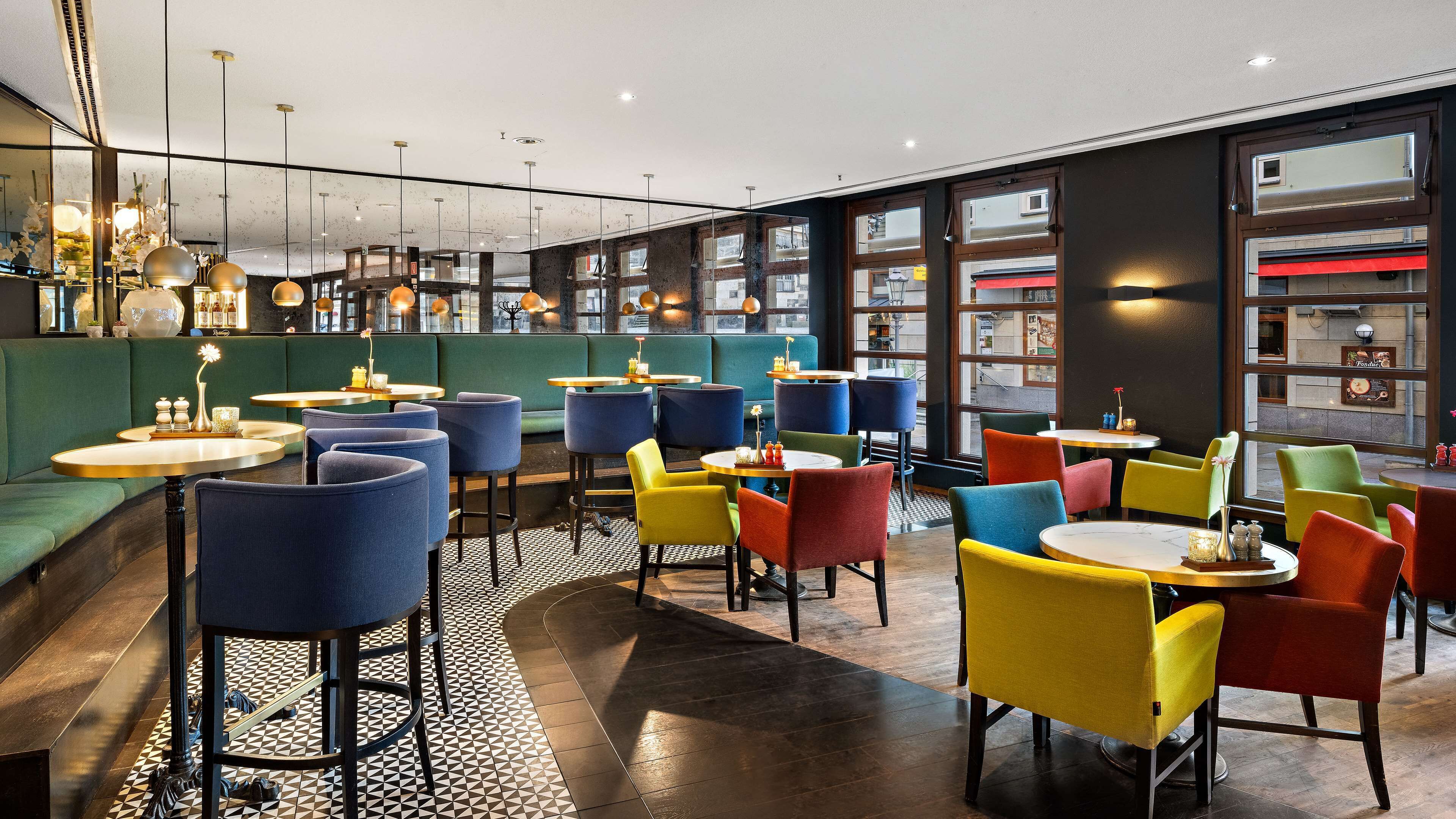 A modern cafe with a variety of seating options including booths and tables, a patterned floor, and large windows offering views of the street.