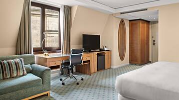 A hotel room with a bed, a desk with a computer, a chair, a sofa, a television, and a wardrobe.