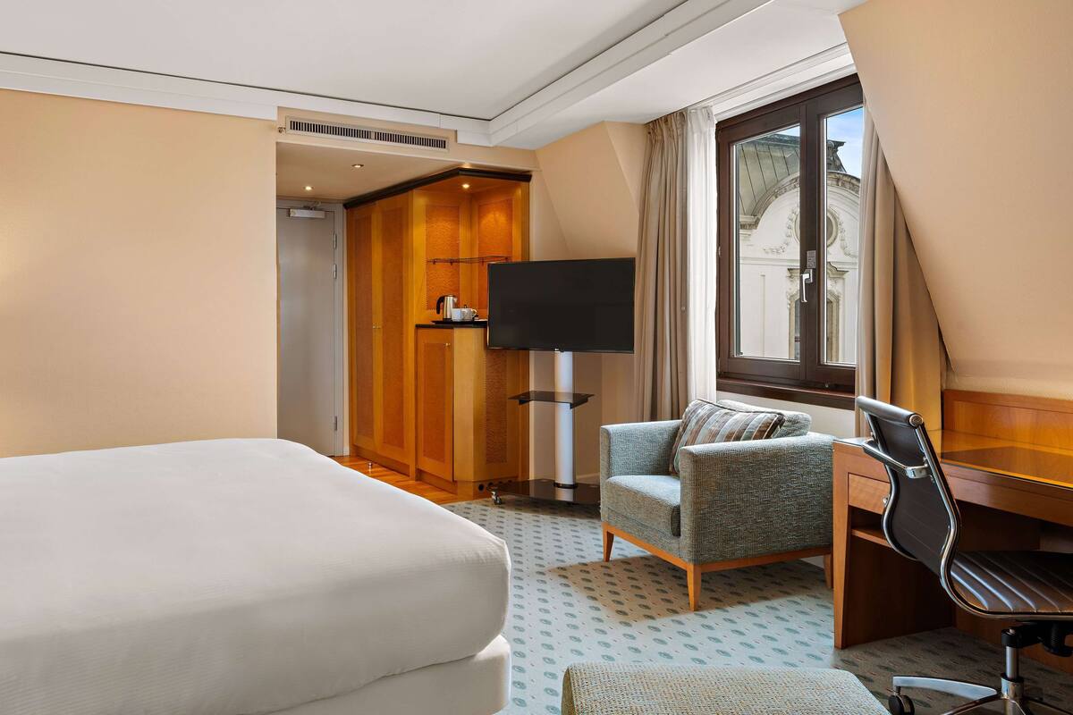 A hotel room with a large bed, a desk with a chair, a television, and a window with curtains.