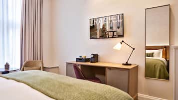 A hotel room with a bed, a desk, a chair, a lamp, and a large mirror.