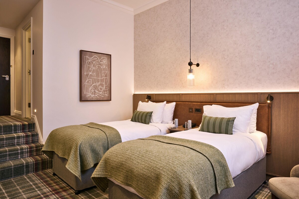 A hotel room with two beds, a staircase, and a framed artwork on the wall.