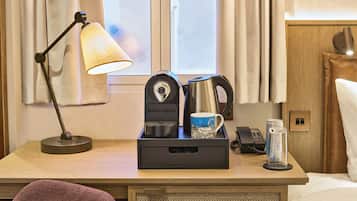 Quarto de hotel com escrivaninha, luminária, cafeteira, caneca, lata e telefone.
