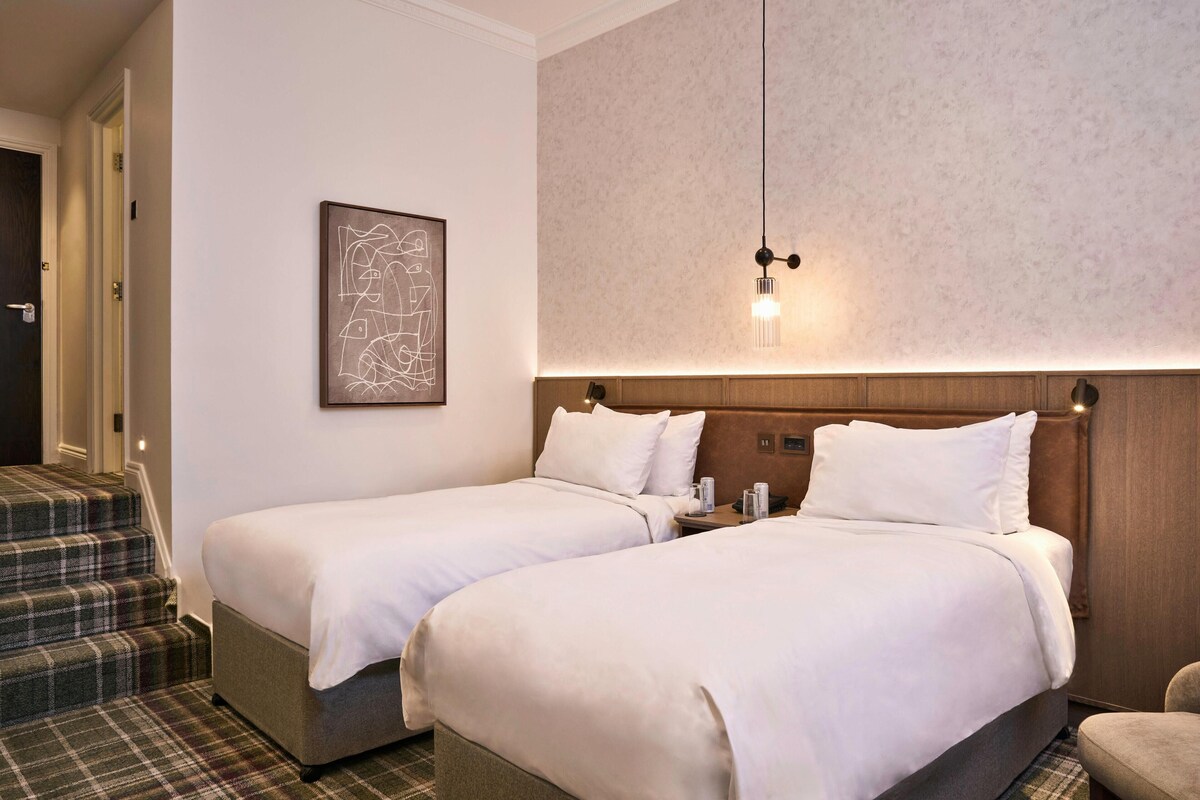 A hotel room with two beds, a staircase, and a wall-mounted artwork.