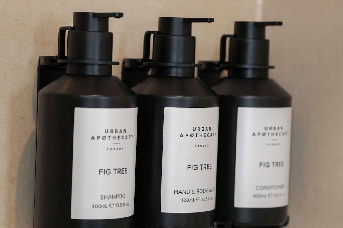 Tres botellas negras de productos Fig Tree de Urban Apothecary sobre una pared de azulejos.
