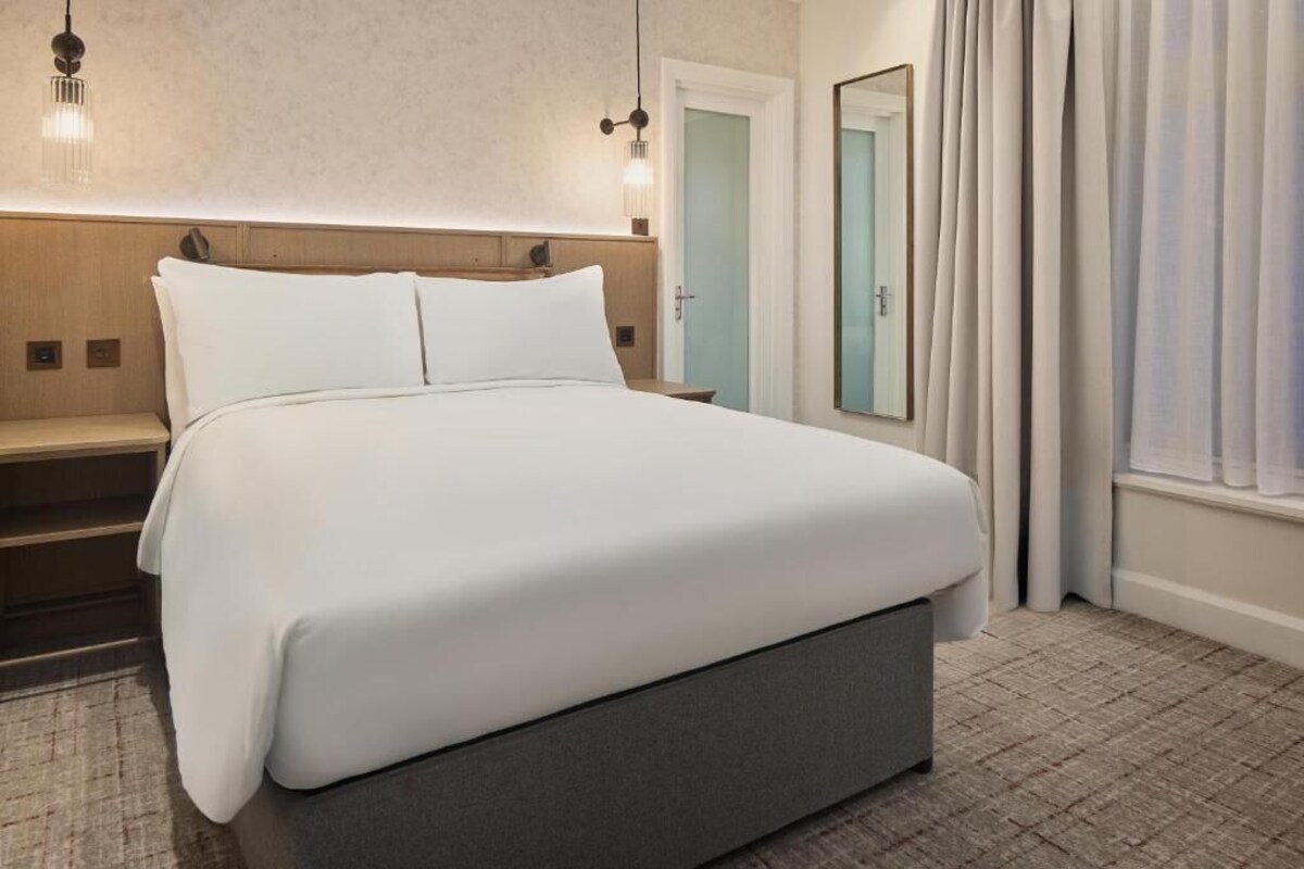 A neatly made bed with white linens, a wooden headboard, and a nightstand with a lamp.