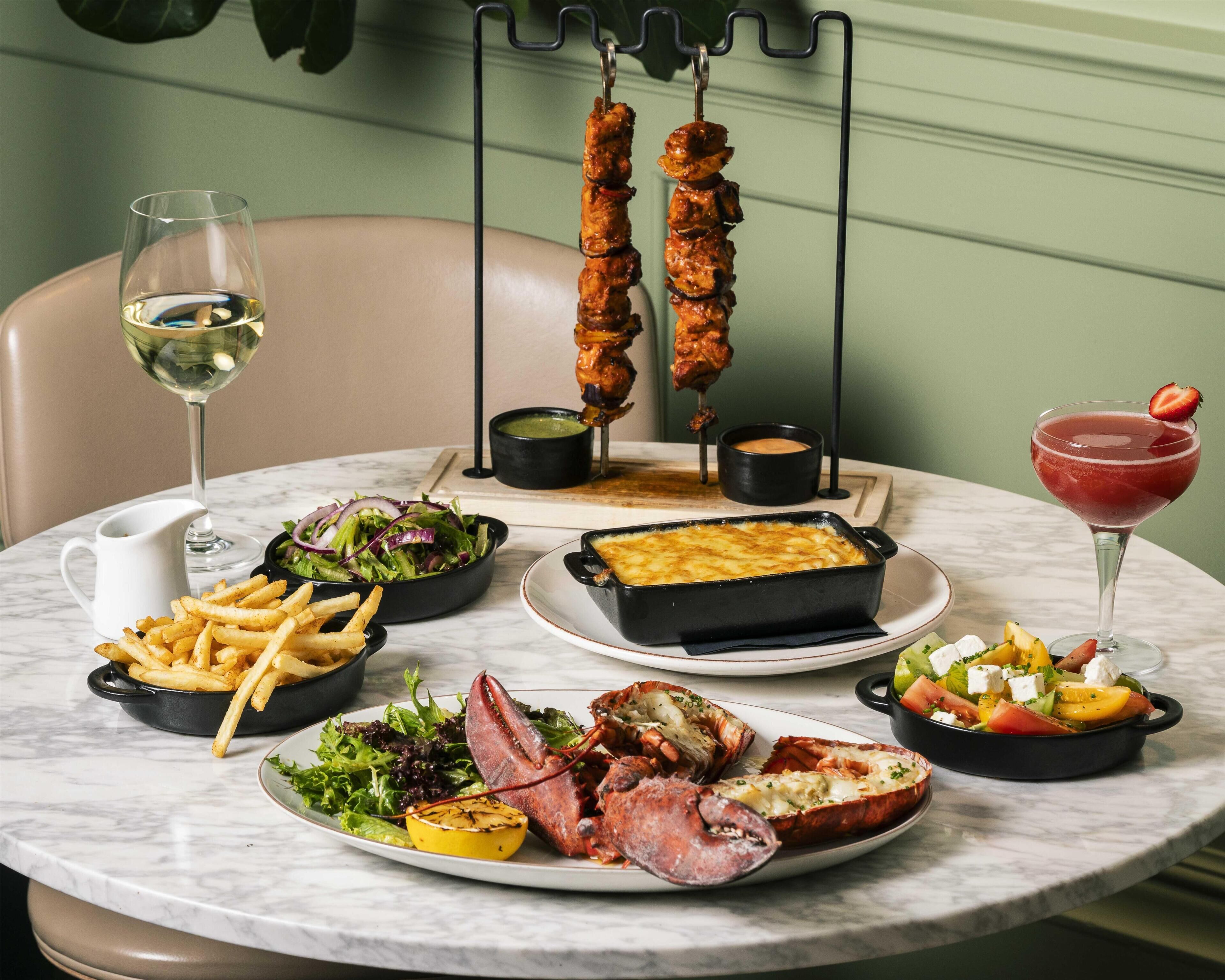 A table set with various dishes including grilled meat, fries, salad, and a dessert.