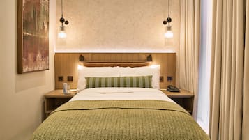 A hotel room with a bed, bedside tables, a nightstand, a telephone, and a painting on the wall.