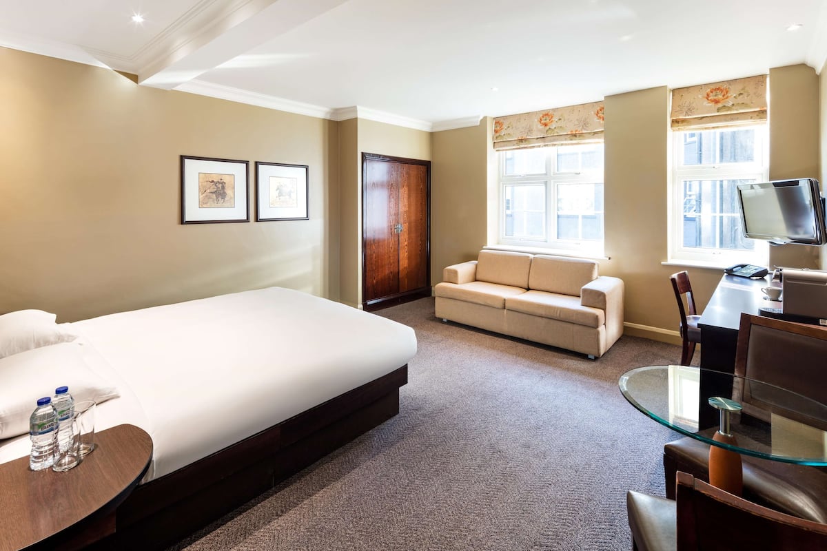 A hotel room with a bed, a sofa, a glass table, and a TV.