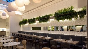 A modern restaurant with round tables, cushioned booths, and hanging plants. - Radisson Blu Hotel, London Euston Square (London)