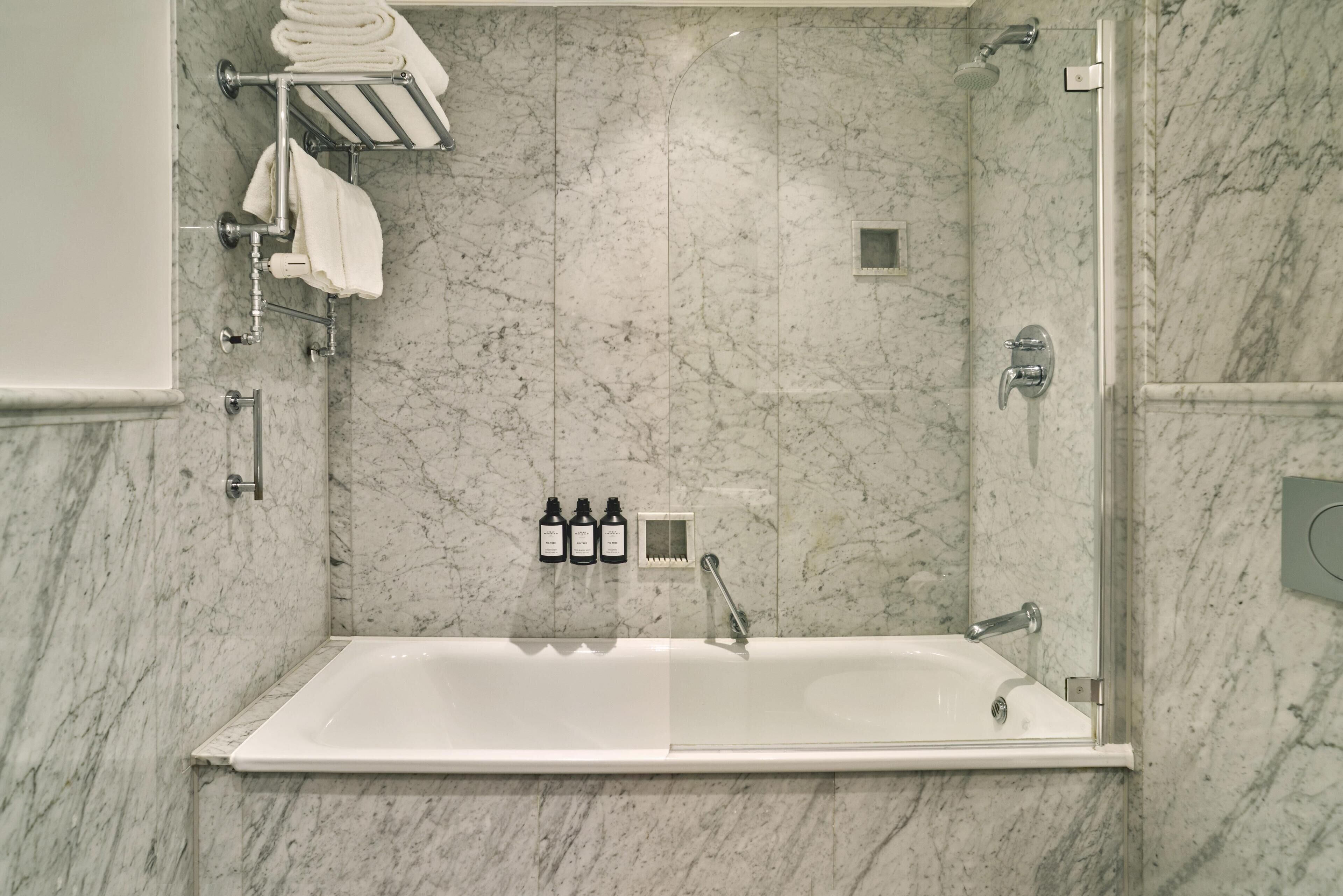 A bathroom with a marble wall, a bathtub, a towel rack, and three bottles of shampoo.