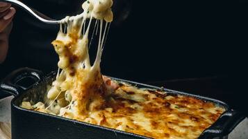 A person lifting a piece of macaroni and cheese from a black baking dish.
