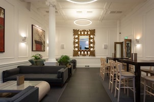 Een moderne lobby met een bank, stoelen, een bijzettafeltje, een grote spiegel en een decoratief raam met uitzicht.