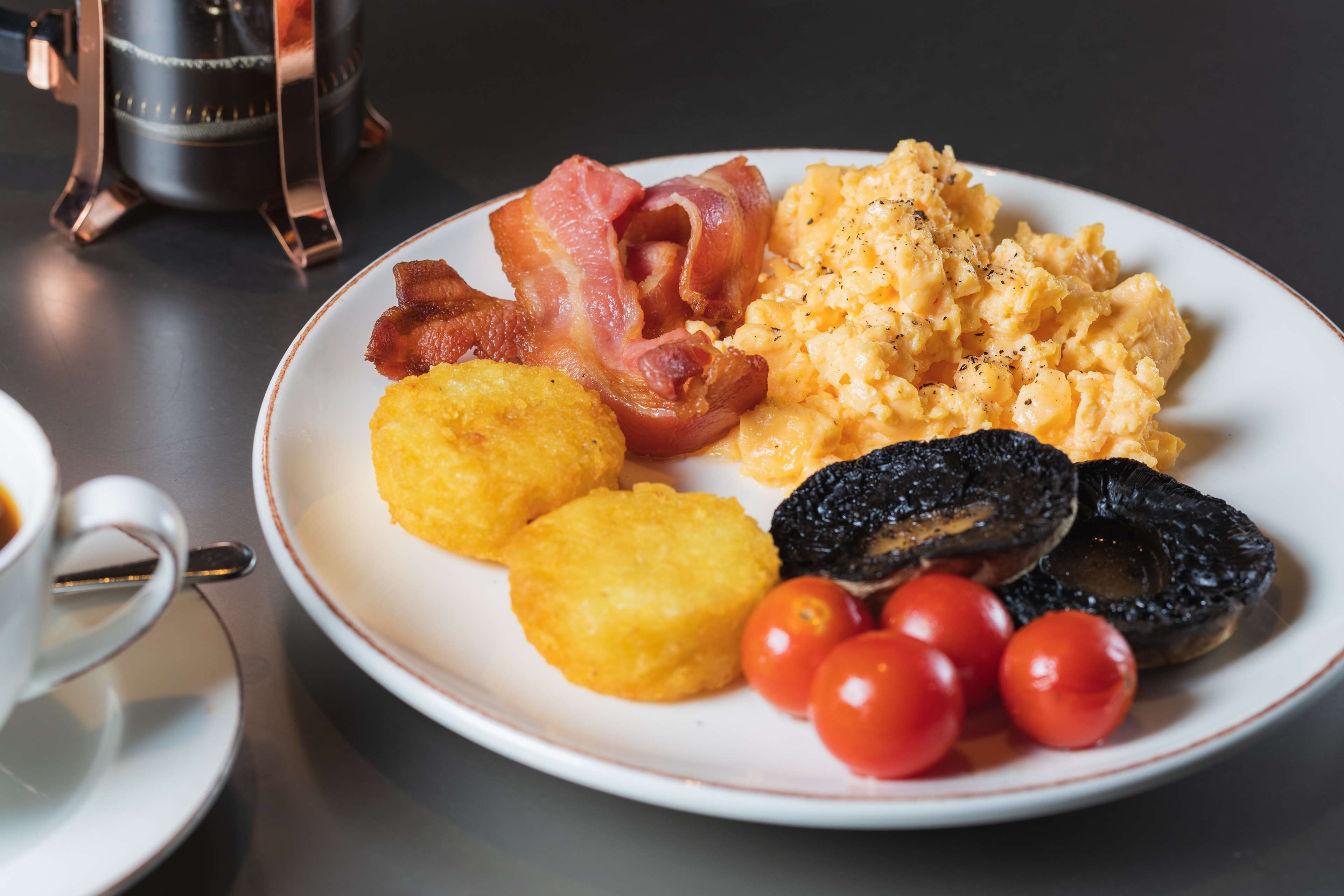 Un plato de comida para el desayuno con huevos revueltos, tocino, harina de maíz, champiñones y tomates cherry.