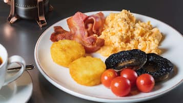 Un plato de comida para el desayuno con huevos revueltos, tocino, harina de maíz, champiñones y tomates cherry.
