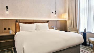 Une chambre d’hôtel avec un grand lit, une tête de lit en bois, une table de chevet avec une lampe, une chaise et une petite table avec une plante.