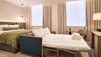 A hotel room with a bed, a desk, a chair, and a small table.