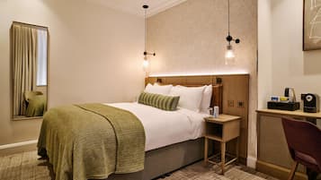 Una habitación de hotel con cama, mesita de noche, lámpara, silla y espejo.
