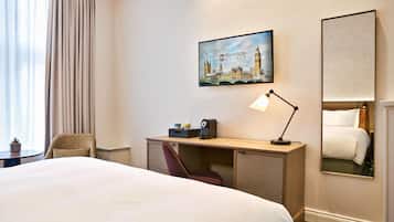 A hotel room with a bed, a desk with a lamp, a chair, a coffee maker, and a painting of a cityscape.