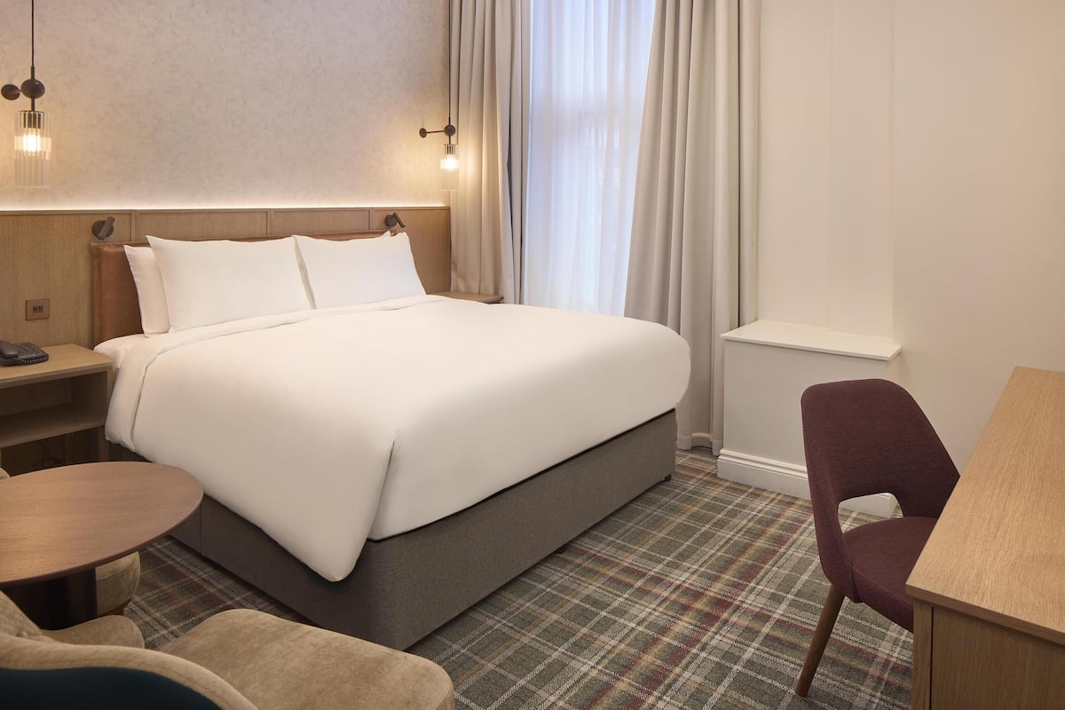 Una habitación de hotel con cama, escritorio, silla y una mesita.