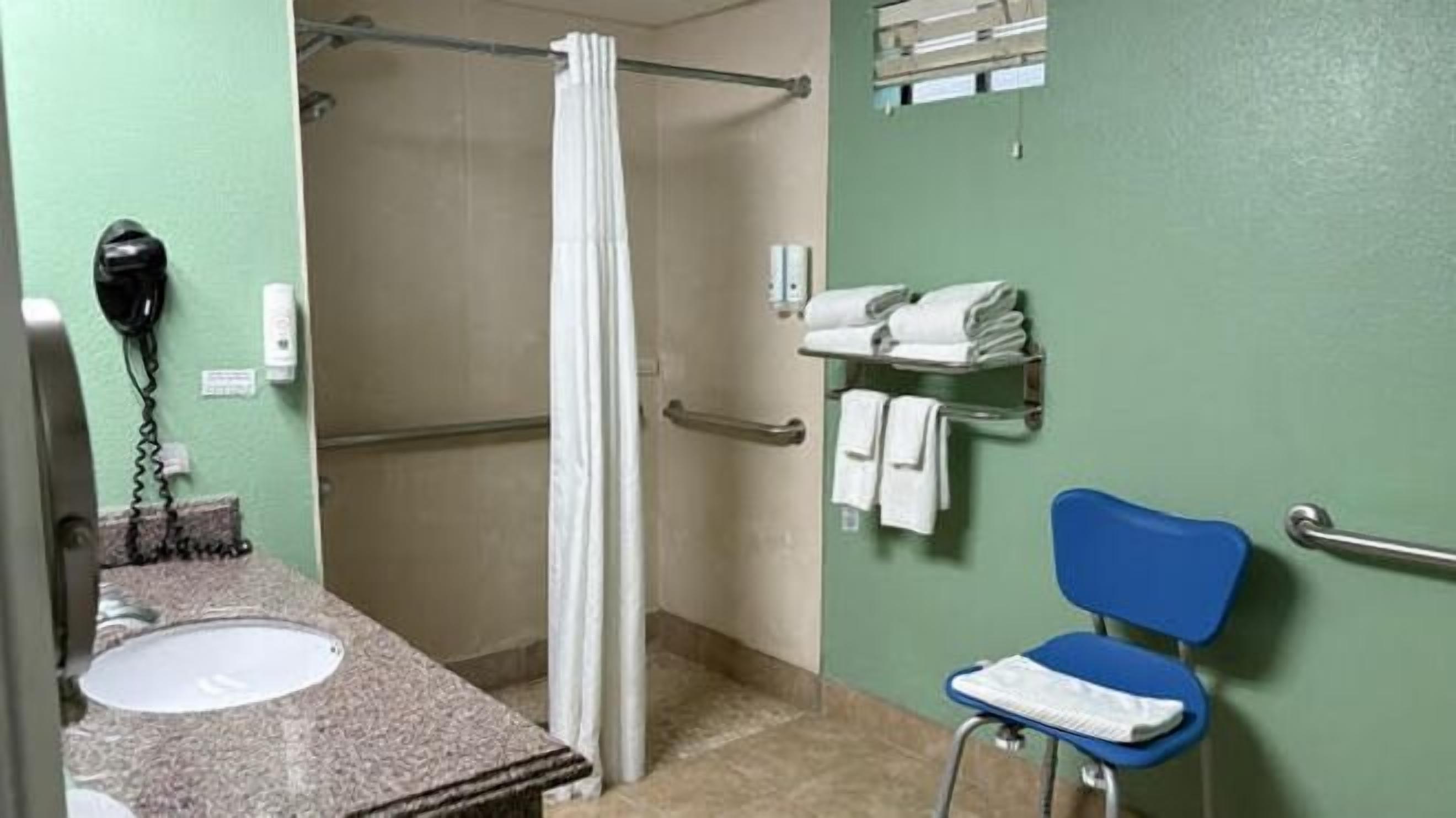 A bathroom with a sink, a shower, a towel rack, and a chair.