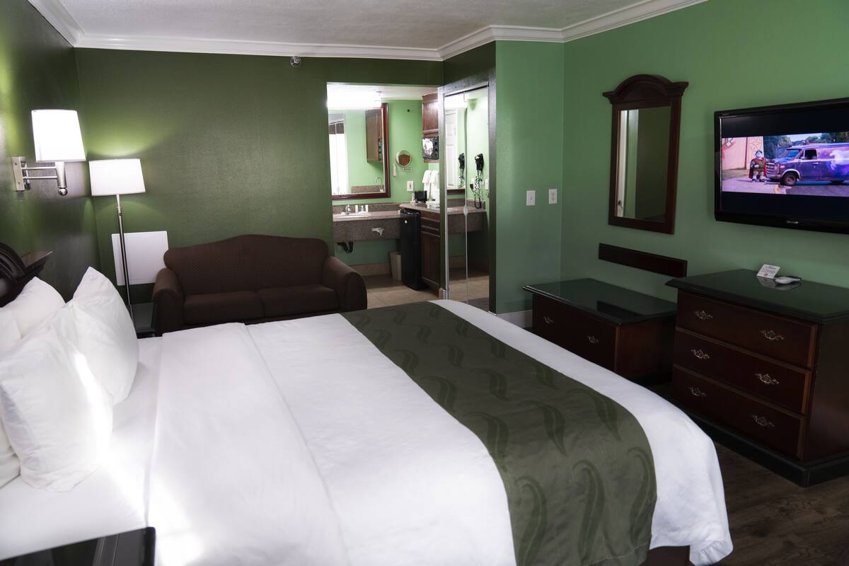 A hotel room with a large bed, a desk, a chair, a television, and a bathroom visible through an open door.