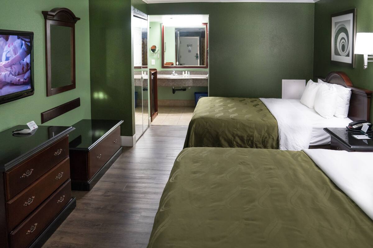 A hotel room with two beds, a TV, a dresser, and a bathroom visible through an open door.