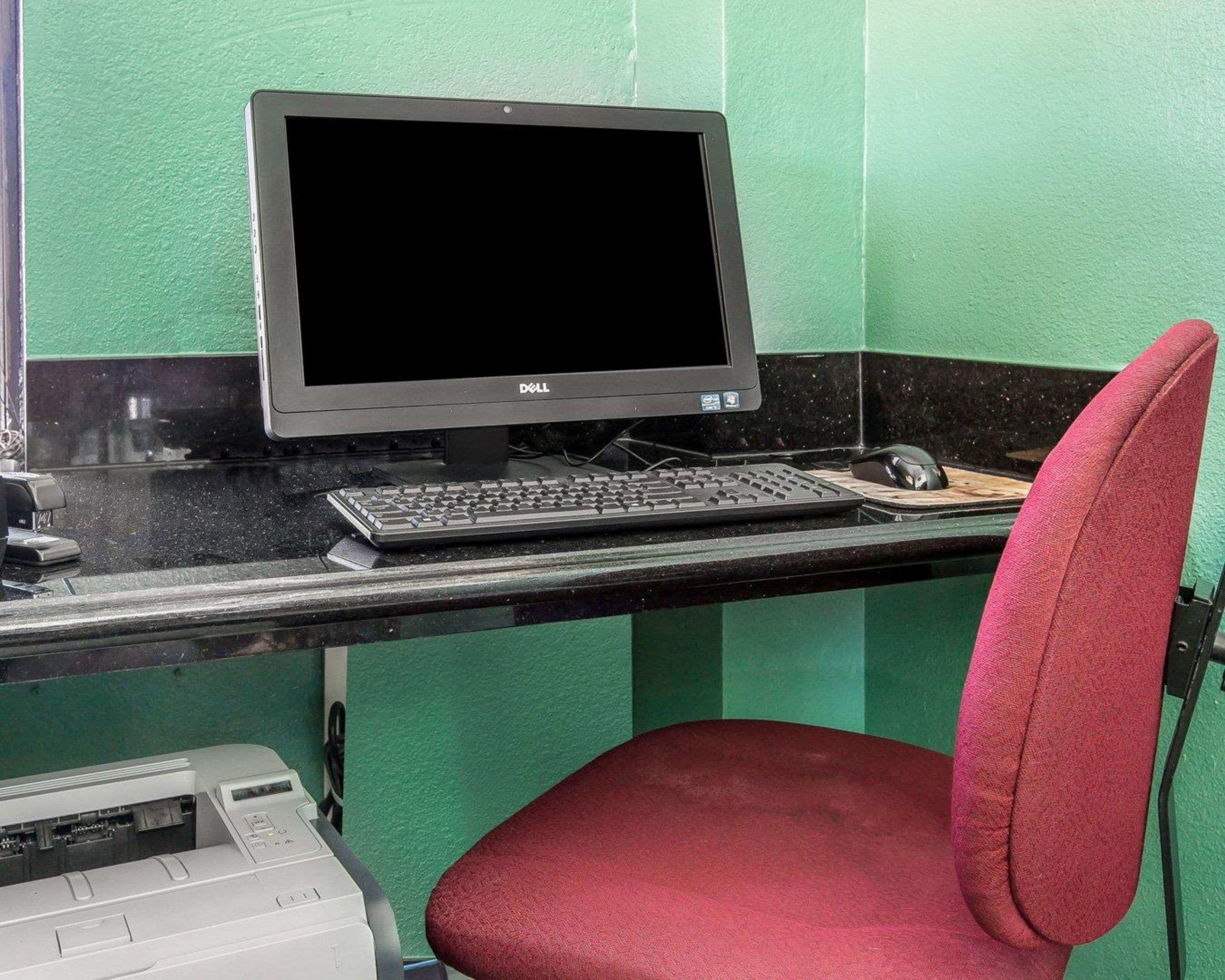 A computer desk with a Dell monitor, keyboard, mouse, and a red chair.
