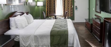 A hotel room with a large bed, a desk, a dresser, a television, and a window with curtains.