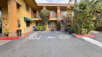 A hotel parking lot with handicapped parking spaces and a building with a yellow facade and a red-tiled roof.