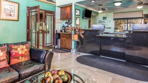 Un hall d’hôtel comprenant un comptoir de réception, un espace où l’on peut se servir du café, un coin salon avec un canapé en cuir et une table basse en verre agrémentée d’objets décoratifs.