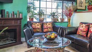 Un salon avec un canapé en cuir, une table basse en verre et une cheminée. On y trouve plusieurs plantes en pot et un tableau encadré accroché au mur.