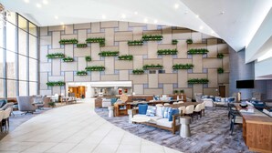 A spacious lobby with a curved ceiling, a central seating area with sofas and chairs, a patterned wall with green plants, and a large window on the left. - Hilton Memphis (Memphis)