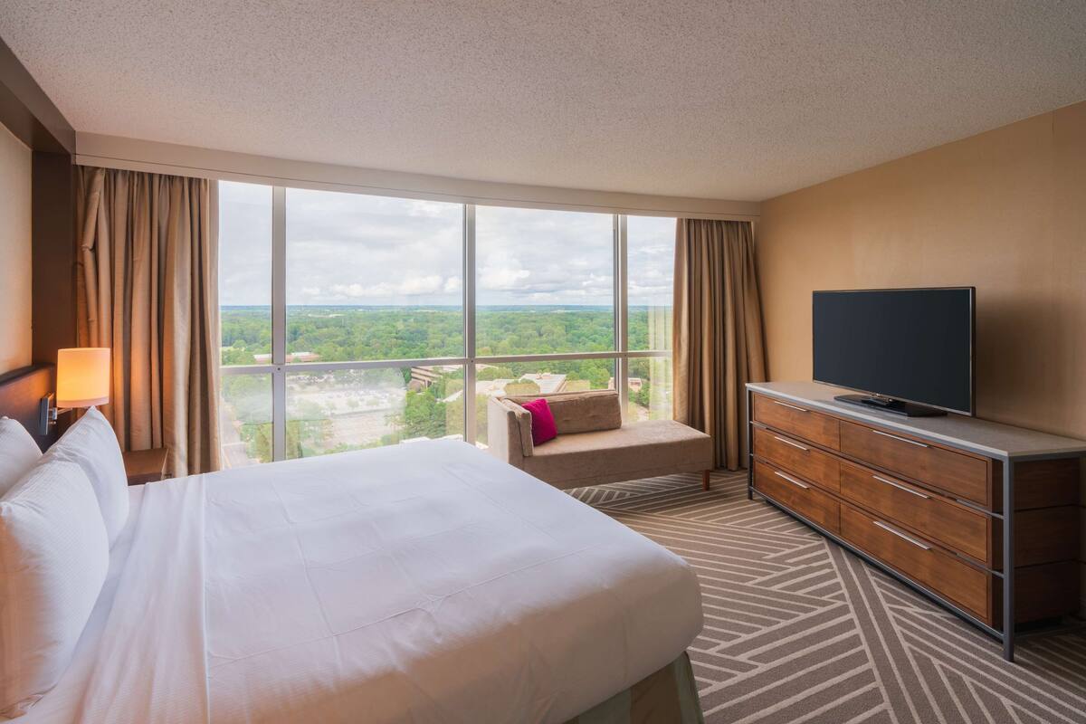 Ein Hotelzimmer mit einem großen Bett, einem Fernseher auf einer Kommode und Blick ins Freie.