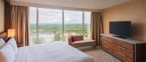 A hotel room with a large bed, a TV on a dresser, and a view of the outdoors.