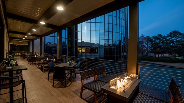 An outdoor dining area with tables and chairs, a fire feature, and a view of the water and buildings. - Hilton Memphis (Memphis)