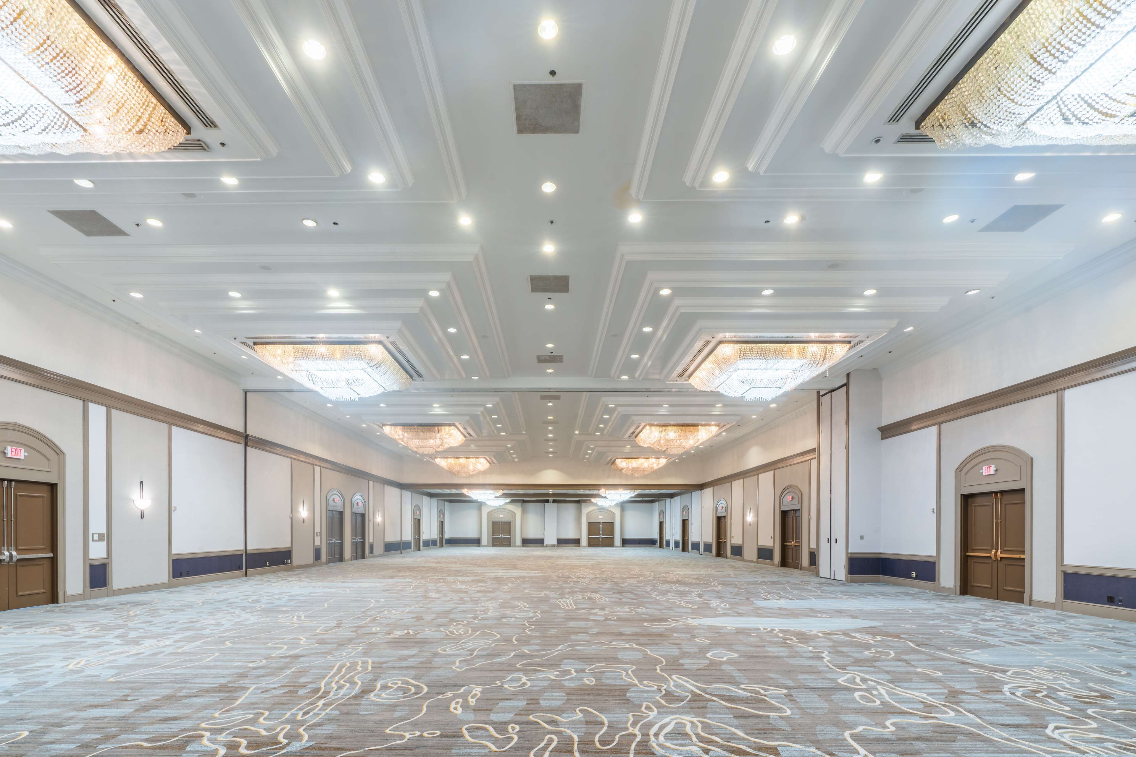 Una sala de conferencias amplia y bien iluminada, con alfombra estampada, iluminación empotrada y puertas simétricas.