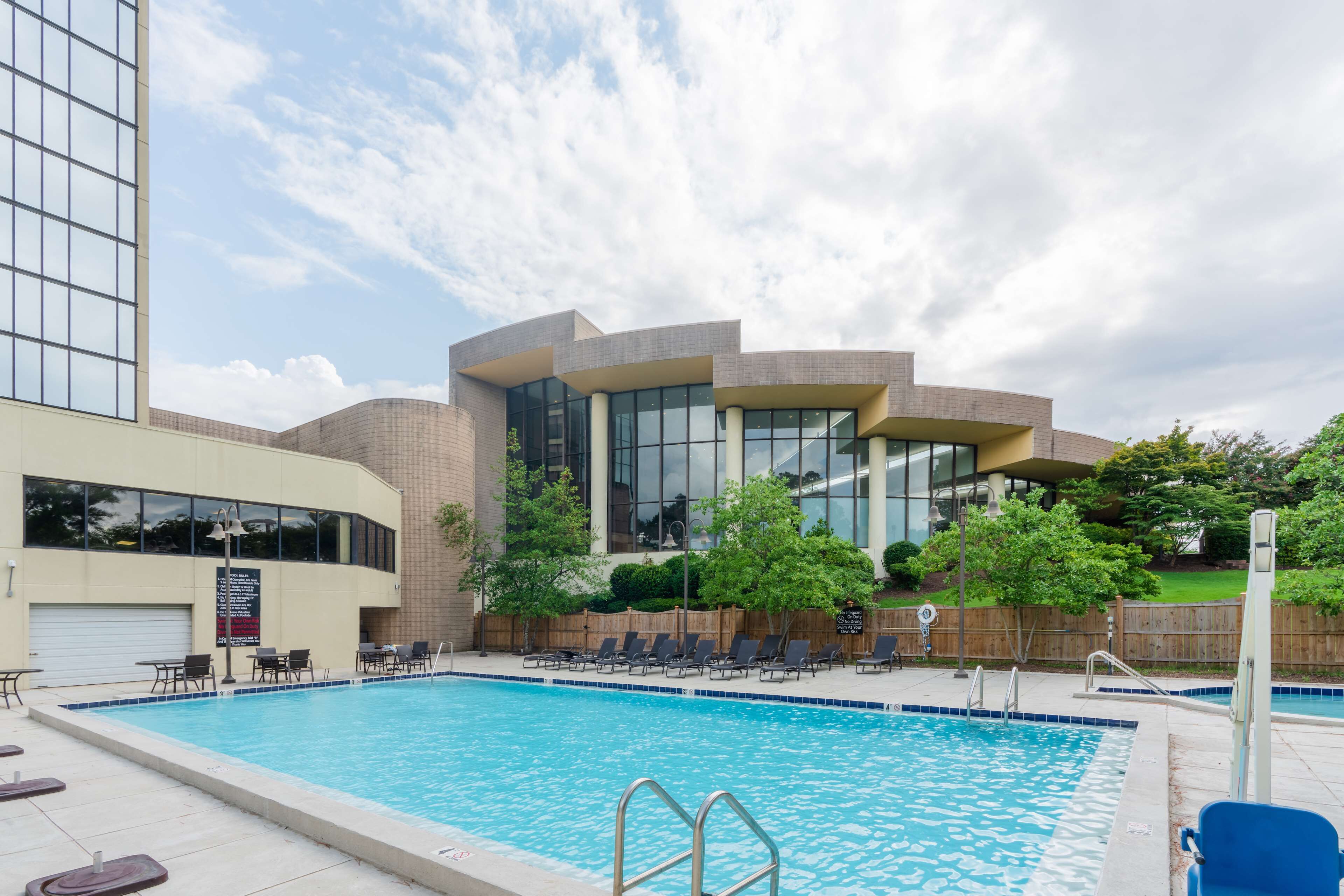 Una piscina con sillones de descanso y un edificio moderno con grandes ventanales al fondo.